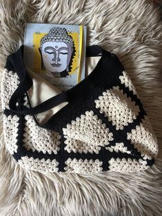 a crocheted bag sitting on top of a fluffy white rug next to a book