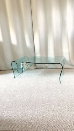 a glass table sitting on top of a carpeted floor next to a white curtain