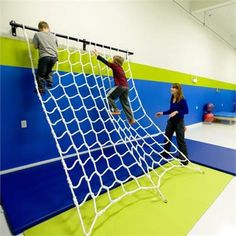 three children climbing on a soccer goal in an indoor gym with blue and green walls