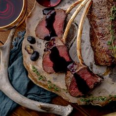 sliced steak on a platter next to some wine and other food items with utensils