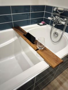 a bathtub with a wine glass and cell phone on the shelf next to it