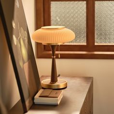 a lamp sitting on top of a wooden table next to a painting and a window