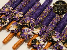 purple and gold candy sticks are arranged on a white tablecloth with flowers in the middle