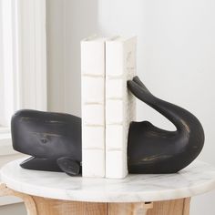 two books are stacked on top of each other in front of a black whale statue