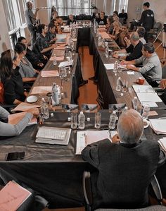 a group of people sitting at long tables with papers and laptops on top of them