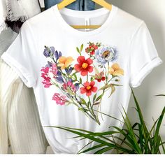 Celebrate the beauty of nature with our Flowers Tshirt. This vintage-inspired botanical tee is perfect for those who adore pastel floral designs and have a deep love for gardens. Embrace the boho wildflowers and Cottagecore aesthetics with this charming shirt. Made from soft and high-quality cotton, our classic unisex jersey short sleeve tee offers a comfortable fit that feels like a well-loved favorite. The ribbed knit collars provide excellent shaping, while the shoulder taping ensures a bette Wildflower Shirts, Cottagecore Printed Summer T-shirt, Cottagecore Summer T-shirt With Plant Print, Botanical Tshirt, Spring Cottagecore T-shirt With Plant Print, Spring Cottagecore Printed T-shirt, Vintage Floral Shirt, Botanical Style Flower Graphic T-shirt, Female Shorts