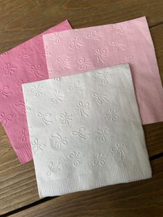 three pink and white napkins sitting on top of a wooden table