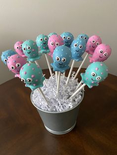 a bucket filled with cake pops covered in blue and pink sprinkles sitting on top of a wooden table