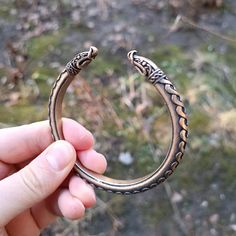 a person is holding an old metal ring in their left hand and it has two snakes on it