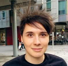 a young man standing in front of a building with his hair blowing in the wind