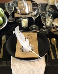 a black plate with a white feather on it next to silverware and wine glasses