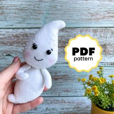 a hand holding a white stuffed animal next to a potted plant with yellow flowers