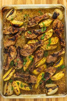 a pan filled with chicken and potatoes on top of a wooden table