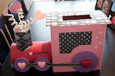 a pink train shaped box sitting on top of a table next to pictures and hearts