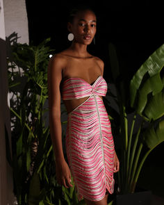 a woman standing in front of a plant wearing a pink dress with cut out sides