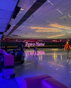 people skating on an indoor ice rink with neon lights hanging from the ceiling above them