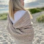 a woman is standing on the beach wearing a shawl