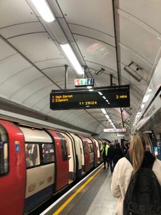 people are walking on the subway platform near an empty train station with signs above them