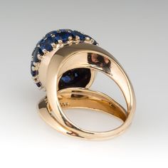 This incredible vintage dome cocktail ring features large blue sapphires with diamonds. The 28 sapphires total 4.7 carats and the three diamonds total .51 carats. The ring dates from the 1940's and features a fantastic split shank design. The ring is crafted of 14k yellow gold and is currently a size 6.75. We offer complimentary resizing to fit. Formal Domed Blue Sapphire Ring, Elegant Blue Dome Ring For Anniversary, Elegant Domed Blue Sapphire Ring, Elegant Blue Domed Sapphire Ring, Luxury Classic Domed Sapphire Ring, Elegant Domed Sapphire Ring In Yellow Gold, Luxury 14k Gold Blue Cluster Ring, Blue Dome Ring For Anniversary - Fine Jewelry, Luxury Gold Domed Sapphire Ring