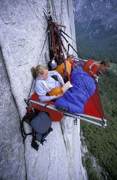 two people are sleeping on the side of a mountain while another person is standing next to them