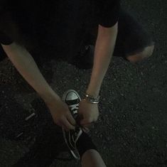 a person tying their shoelaces to another persons shoes on the street at night