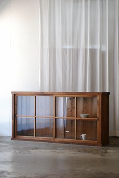 a wooden cabinet with glass doors in front of a white curtained wall and floor