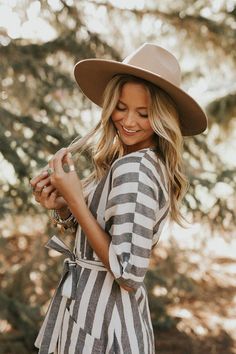 a woman wearing a brown hat and striped dress in the woods with her hand on her hip