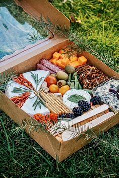 a wooden box filled with assorted cheeses and meats on top of grass