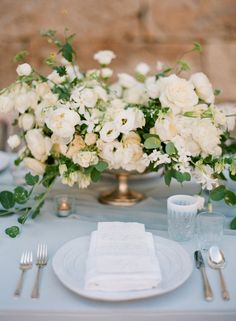 the table is set with white flowers and silverware