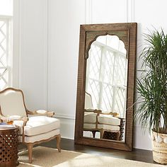 a mirror sitting on top of a wooden floor next to a chair and potted plant