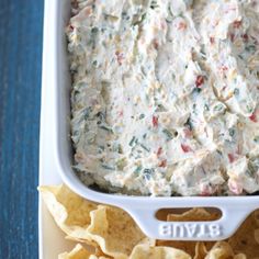 a white casserole dish filled with dip and tortilla chips on a blue table