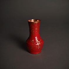 a red vase with gold speckles on it sitting on a black surface in front of a gray background