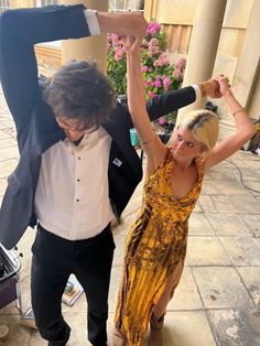 a man and woman dancing on the sidewalk in formal wear with their arms up to each other