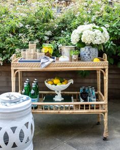 a wicker bar cart with lemons and bottles on it in front of some bushes