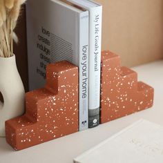 two books are stacked on top of each other next to a vase with dried flowers