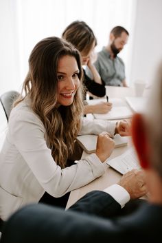 a woman sitting at a table in front of two other people working on papers and laptops