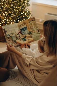 a woman sitting on the floor reading a book with a christmas tree in the background