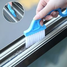 a hand holding a blue brush on top of a window sill next to a window