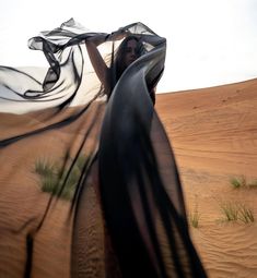 a woman is standing in the desert with her long black dress blowing in the wind