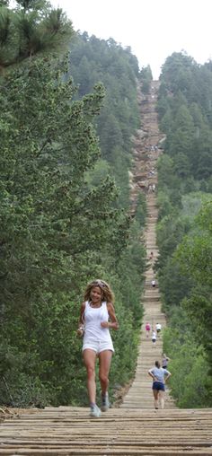 a woman is running down a wooden path in the woods while another person runs behind her