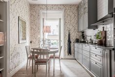 a dining room table and chairs in front of an open kitchen door with floral wallpaper