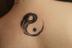 the back of a woman's shoulder with a yin symbol tattoo on her left side