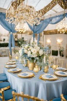 a table set with blue and gold place settings, candles, and centerpieces