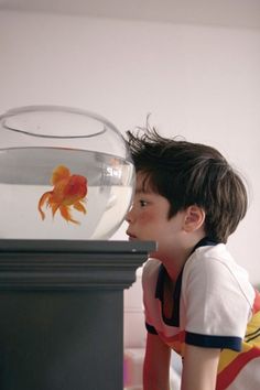 a young boy looking at a goldfish in an aquarium