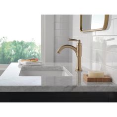 a bathroom sink with a gold faucet and marble counter top next to a window