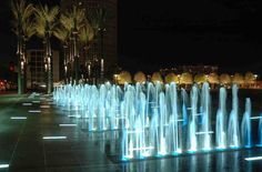 the fountains are lit up at night in front of palm trees