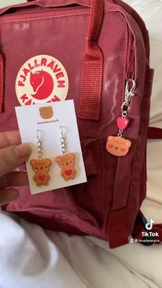 someone is holding onto some cute little bear earring set in their hand and it's attached to a red backpack