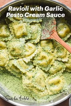 a pot filled with pasta and pesto sauce on top of a wooden table next to a spoon