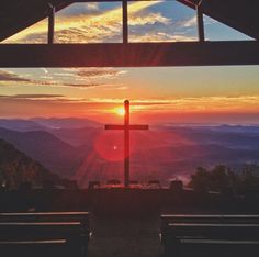 the sun is setting behind a cross on top of a hill with mountains in the background