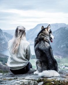 a woman sitting on top of a rock next to a dog looking at the mountains